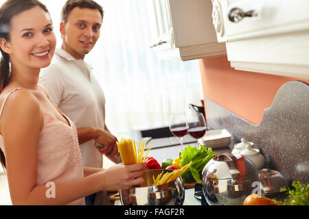 Young woman cooking spaghetti while her husband cutting vegetables Stock Photo