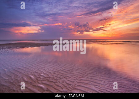 Spectacular sunset colours over sea reflected in the water at low tide. Photographed on the island of Texel, The Netherlands. Stock Photo