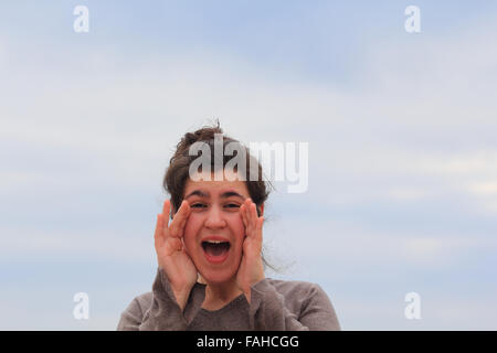 Young woman shouting, with hands on mouth Stock Photo