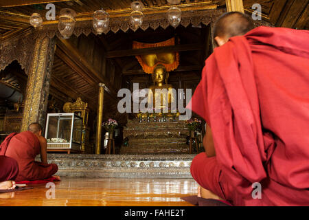 Buddhist monks in prayer at Shwe Yan Pyay Monastery at Taunggyi, Myanmar (Burma). A golden Buddha statue sits at the altar. Stock Photo