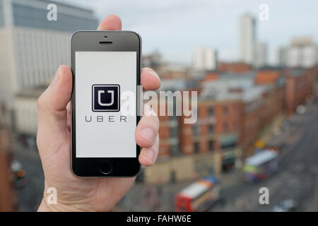 A man uses the Uber taxi smartphone app while stood in a tall building overlooking a busy city street (Editorial use only) Stock Photo