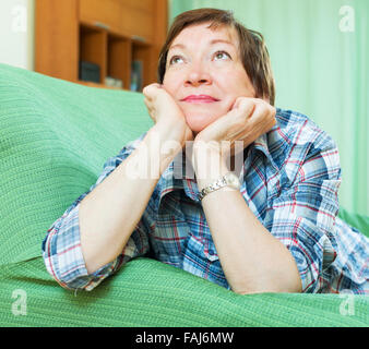 Stressed elderly female laying on her elbows and thinking indoor Stock Photo