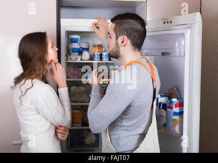 Housewife showing broken refrigerator to serious repairman Stock Photo