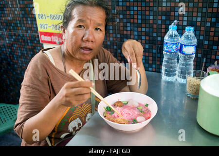 Thai food. Old woman eating pink noodles. Market stall and street food being prepared in Chinatown Bangkok, Thailand. Yaowarat, Stock Photo