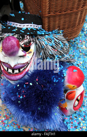 two basel carnival masks lay on the ground covered with blue confetti besides a basket Stock Photo