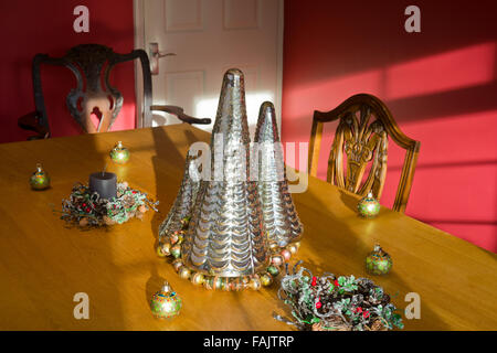 Christmas decorations. Christmas tree shaped silver glass decorations on a table top, with baubles and candle. Stock Photo