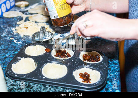 Making mince pies adding mincemeat to pastry cases cooking in kitchen baking tray Stock Photo