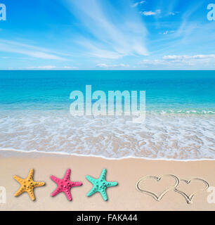 turquoise water and golden sand in Sardinia with two hearts drawn in the sand and three colorful starfish Stock Photo