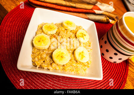 A bowl of oatmeal with banana slices and cinnamon on a round placemat on a wooden table Stock Photo