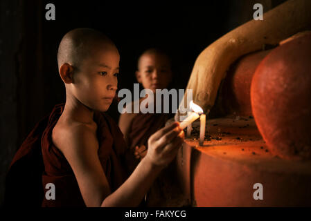 Portrait of young novice monks lighting up candlelight inside a Buddhist temple, low light setting, Bagan, Myanmar. Stock Photo