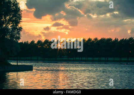 The sun setting behind trees on a lakeside Stock Photo