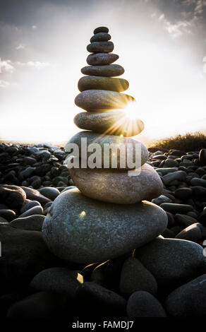 Morning sunlight shining through a stack of pebbles on a beach. Stock Photo