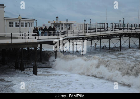 People stand on Worthing Pier and watch the large waves crash onto the beach on New Years Day in Worthing, West Sussex, England. Stock Photo