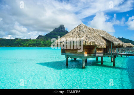 Luxury overwater thatched roof bungalow in a honeymoon vacation resort in the clear blue lagoon of Bora Bora near Tahiti. Stock Photo