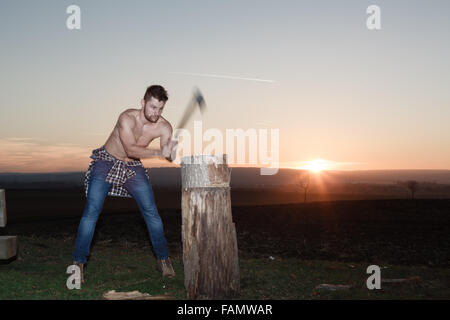 The stylish lumberjack chopping wood at sunset. (Motion blur axe). Stock Photo