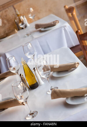 Simple Table setting in a restaurant with white tablecloth napkins and wine glasses. Stock Photo