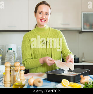 Smiling russian woman preparing slices of white fish for baking Stock Photo