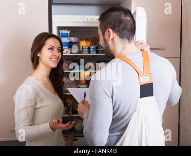 Young housewife showing broken refrigerator to repairman Stock Photo