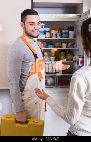 Young housewife showing broken refrigerator to positive repairman Stock Photo