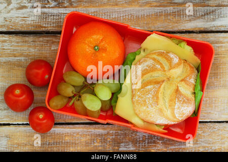 Lunch box containing cheese roll, mandarine, grapes and cherry tomatoes on rustic wooden surface Stock Photo