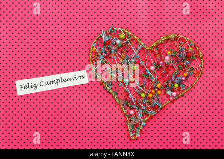 Feliz Cumpleanos (Happy Birthday in Spanish) card with heart made of colorful beads on dotty pink surface Stock Photo