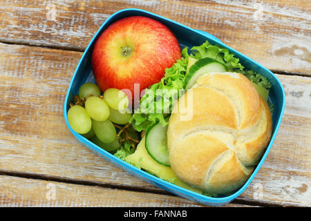 Lunch box containing bread roll with cheese, lettuce and cucumber, red apple on rustic wood Stock Photo