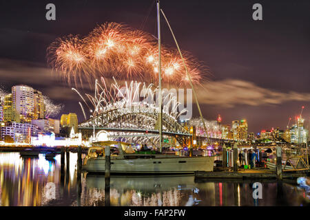 brightly lit city of Sydney during new year night and fireworks over Sydney Harbour Bridge reflecting in still waters Stock Photo