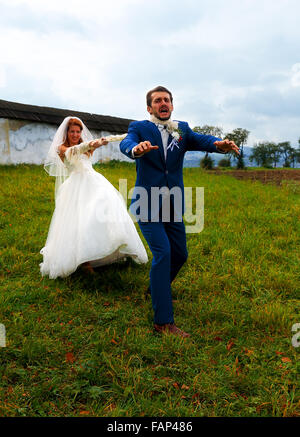 bride pulling her groom to her with a rope - funny wedding concept Stock Photo