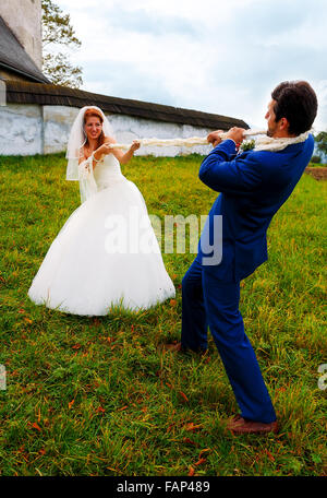 bride pulling her groom to her with a rope - funny wedding concept Stock Photo