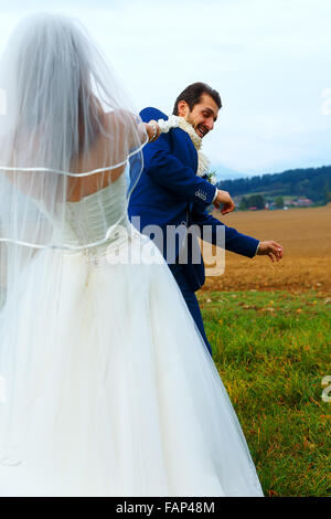 bride pulling her groom to her with a rope - funny wedding concept Stock Photo