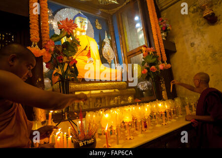 Monks offering praying candles in front of golden Buddha statue inside Mahabodhi temple chamber in Bodh Gaya, Bihar, India. Stock Photo