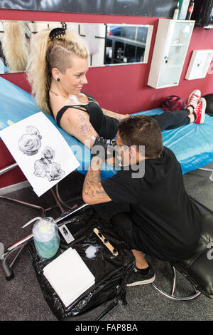 Aesch, Switzerland. 14th Aug, 2015. Dennis Weber (R), a man with dwarfism, tattooes Ramona Hopfner in a tattoo studio in Aesch, Switzerland, 14 August 2015. Many people with dwarfism face problems when looking for a job. Photo: PATRICK SEEGER/dpa/Alamy Live News Stock Photo