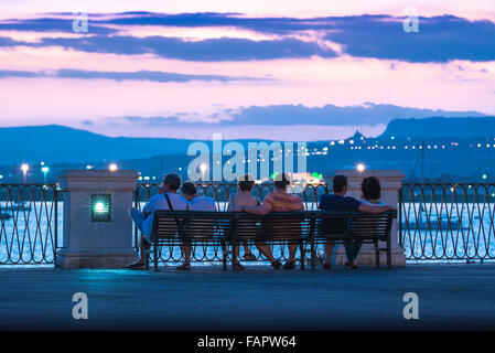Syracuse Sicily bay, on a summer evening a group of tourists watch the remains of a colourful sunset over the harbour in Syracuse, Sicily. Stock Photo