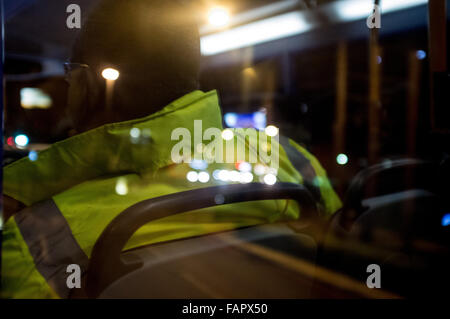 Lights reflected in construction worker's yellow reflective jacket on the top deck of a bus. Stock Photo