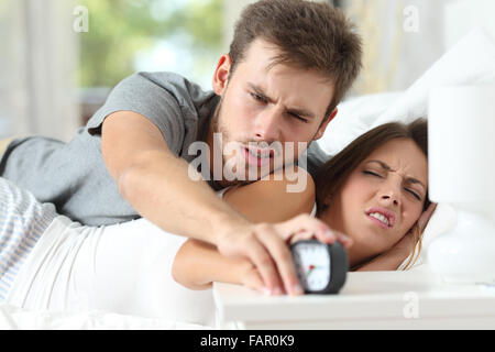 Sleepy angry couple in the bed turning off the alarm clock in the morning Stock Photo