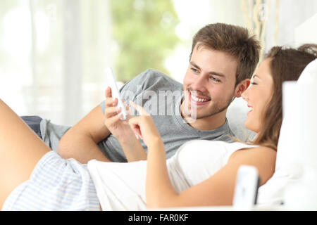 Happy marriage sharing a smart phone on the bed at home Stock Photo