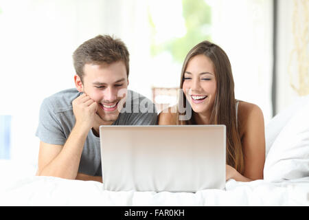 Front view of a couple laughing while watching media on a laptop at home Stock Photo