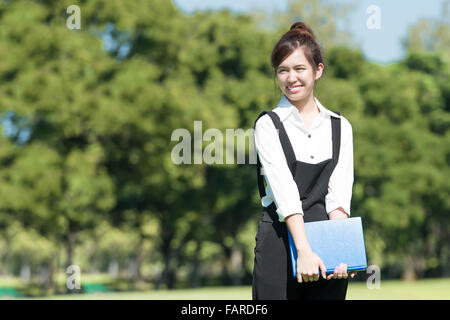 Asian student holding books and smiling while standing in park at college Stock Photo