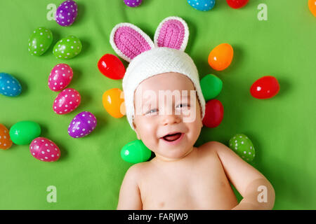 Baby boy in bunny hat lying on green blanket with easter eggs Stock Photo