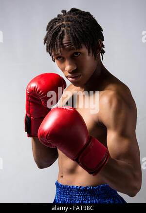 Young muscular athletic male boxer wearing blue boxing shorts and red boxing gloves. Stock Photo