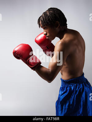 Young muscular athletic male boxer wearing blue boxing shorts and red boxing gloves. Stock Photo