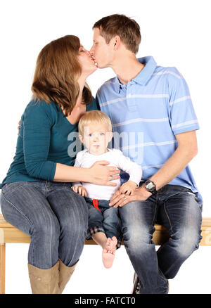 Caucasian family with mom dad and baby boy. They are all wearing denim jeans and sitting on a wooden bench. The parents are kiss Stock Photo