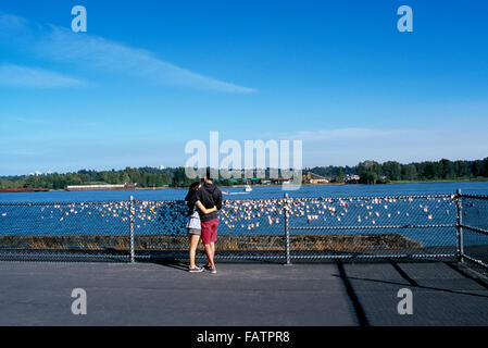 Young Couple in Love, Lovers attaching Love Lock / Locks on Fence along Fraser River, New Westminster, British Columbia, Canada Stock Photo