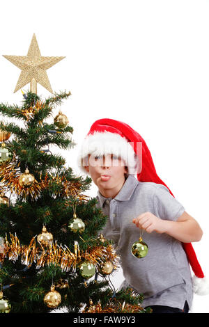 Boy with santa hat sticking out tongue at  the Christmas tree on white background Stock Photo
