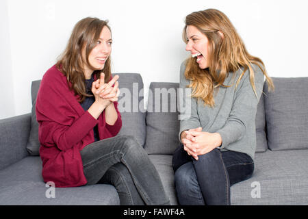 Two female friends having fun while sitting on coach in the living room Stock Photo