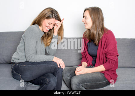 Two female friends having fun while sitting on coach in the living room Stock Photo