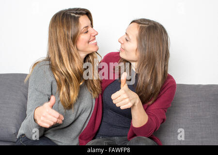 Two female friends having fun while sitting on coach in the living room Stock Photo