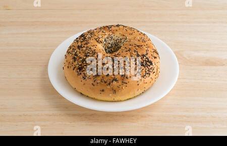 A bagel with several different types of seasonings on a white plate atop a wood table top. Stock Photo