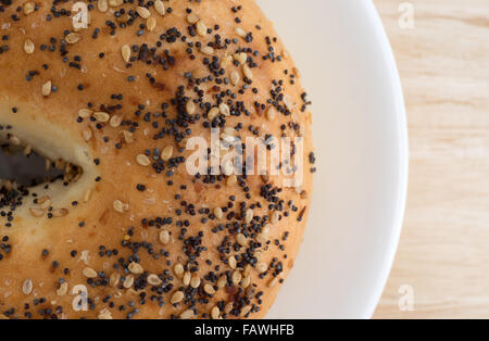 Top close view of a bagel with several different types of seasonings on a white plate atop a wood table top. Stock Photo