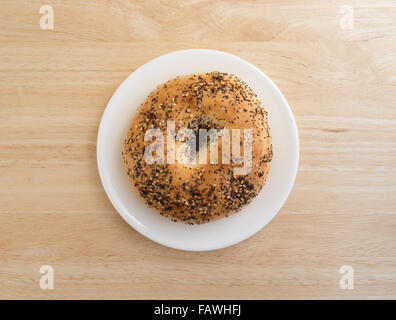 Top view of a bagel with several different types of seasonings on a white plate atop a wood table top. Stock Photo